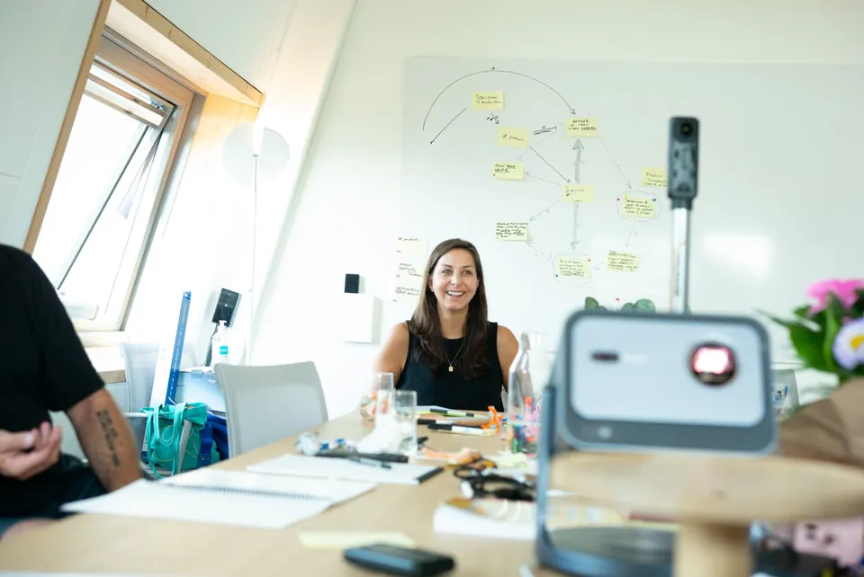 Kristin Walter am Workshoptisch mit Team, im Hintergrund ein Whiteboard mit Haftnotizen